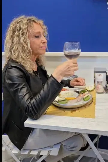 Cliente seduta al tavolo della pescheria, con un calice di vino e un piatto di crudo